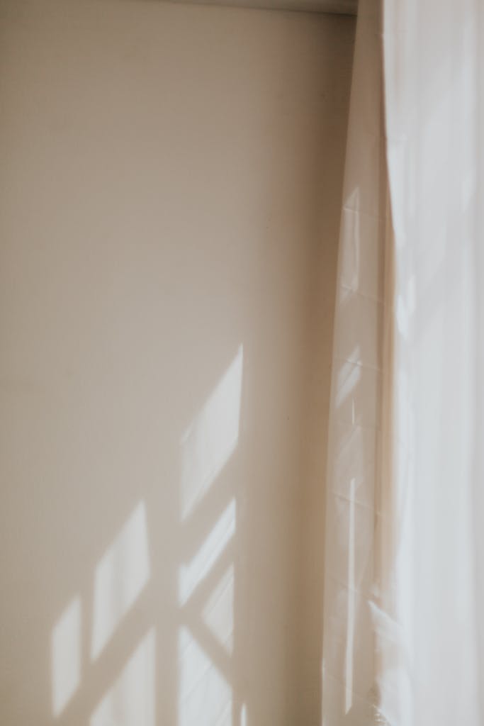 Una serena escena de interior con luces y sombras que juegan sobre una cortina y una pared.